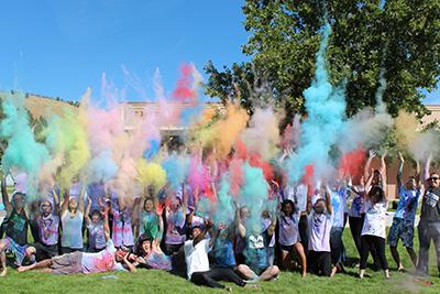 Students gathered on lawn throwing multi colored power in the air. 