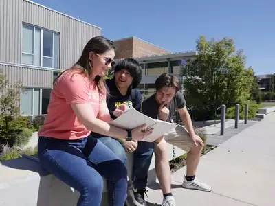 Students and counselor sitting on a low concrete wall talking, looking at information in a binder